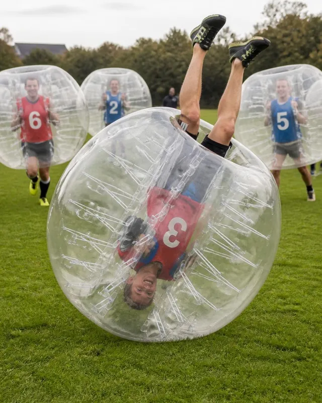 En vuxen spelare ligger upp och ned i en genomskinlig bumperball medan laget står bakom.