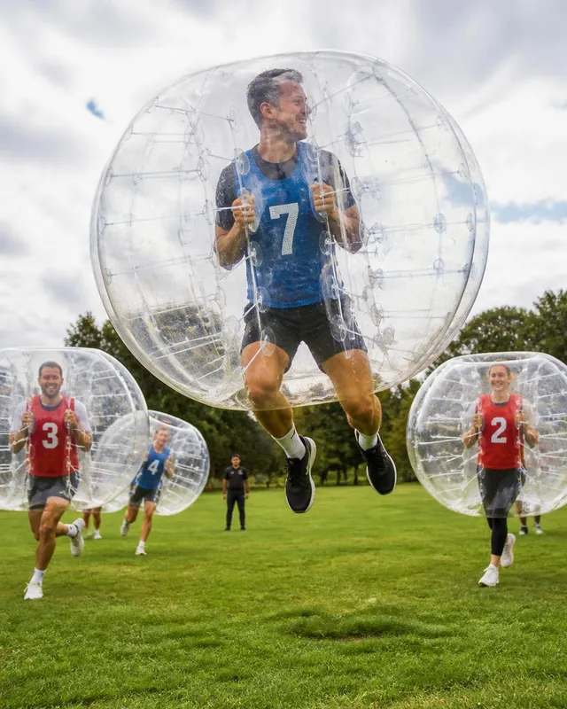 En vuxen i blå väst hoppar med sin bumperball på gräsmattan.