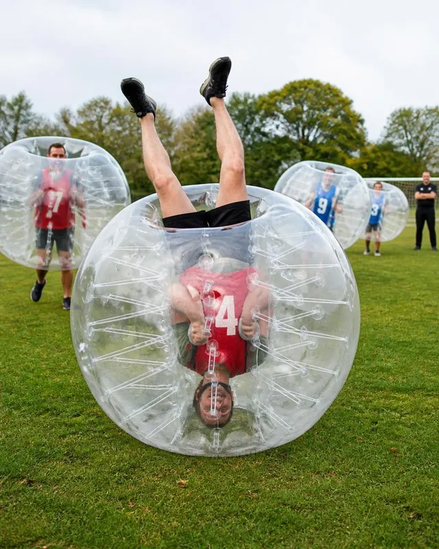 En vuxen i röd väst rullar upp och ned i en genomskinlig bumperball på gräs.