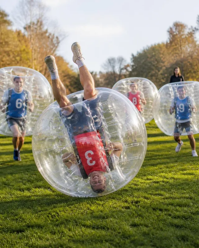 En vuxen spelare rullar upp och ned i en bumperball med laget i bakgrunden.