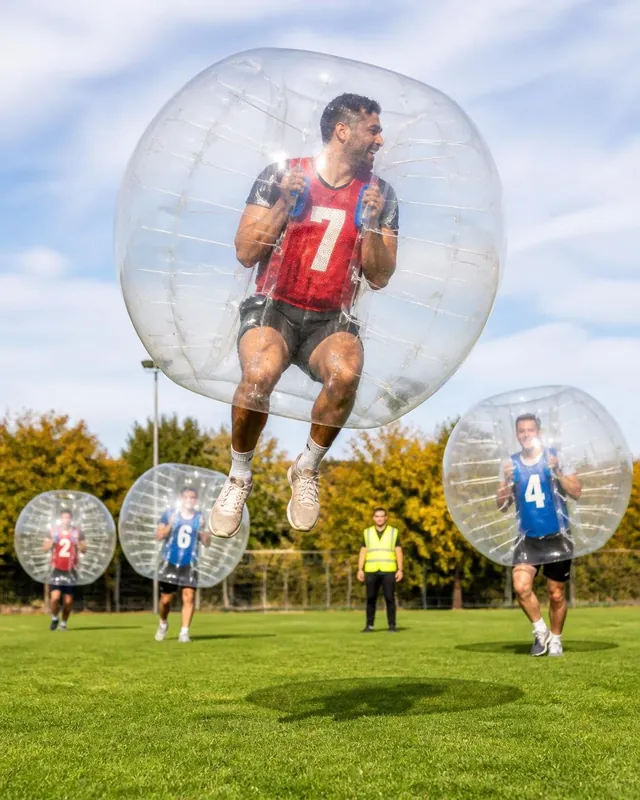 En vuxen i röd väst hoppar högt i en bumperball på en gräsmatta.