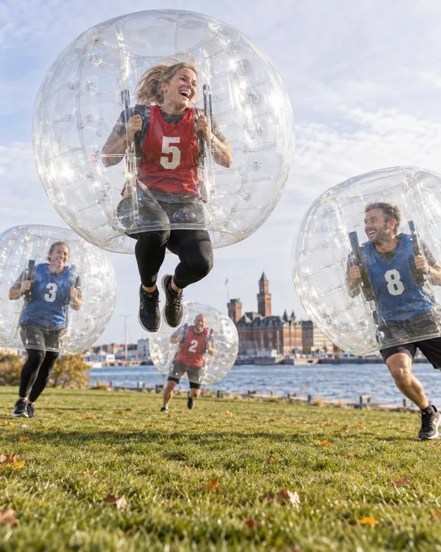 En vuxen i röd väst hoppar med en genomskinlig bumperball utomhus.
